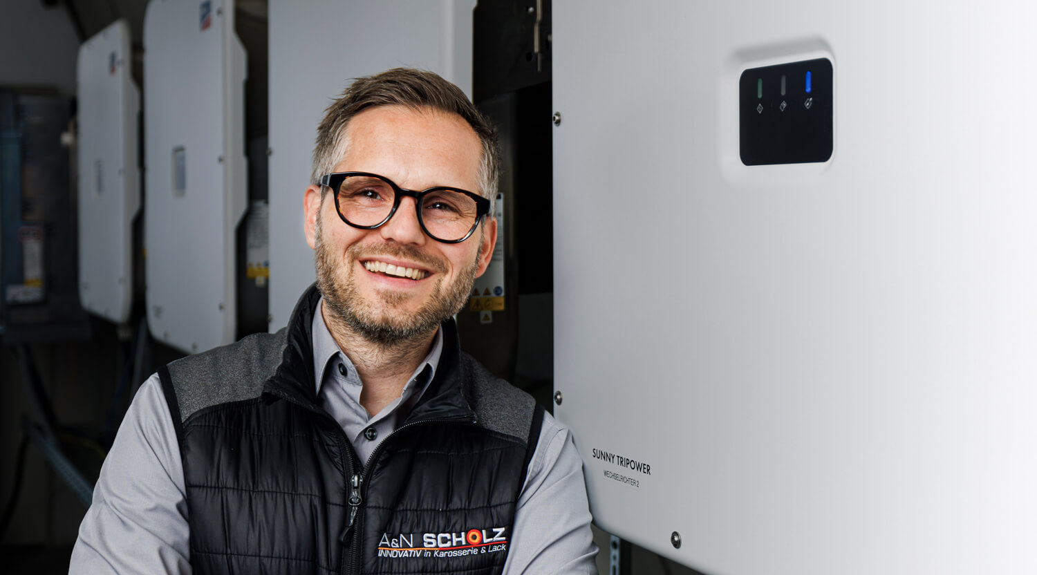 Ein Mann steht vor einer Infografik, die ein Energiekonzept mit Photovoltaikanlage, Batteriespeicher und Energieflüssen zwischen Gebäude, Netz und Verbrauchern zeigt